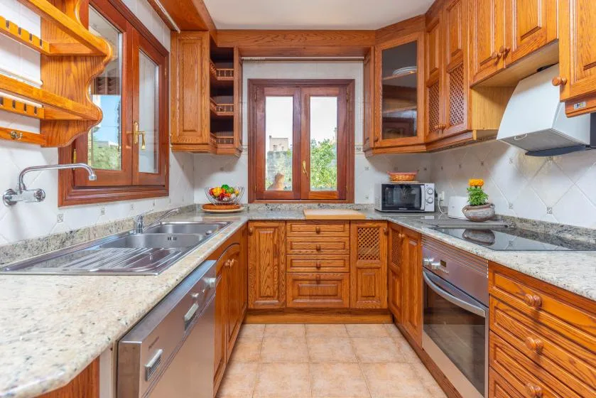 Una cocina con gabinetes de madera, fregadero, encimera y ventana central.
