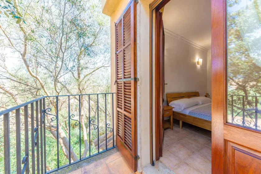 Un dormitorio se abre a un balcón con barandilla metálica y árboles alrededor.