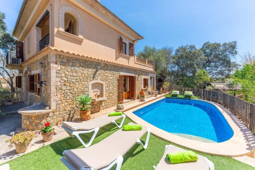 A two-story house beside a swimming pool and lounge chairs.