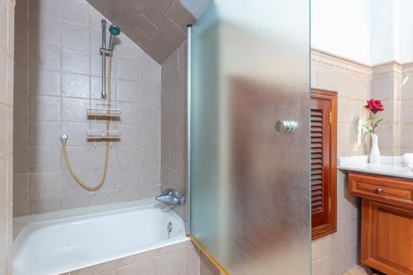 Un baño con azulejos, bañera, ducha y mueble de madera.
