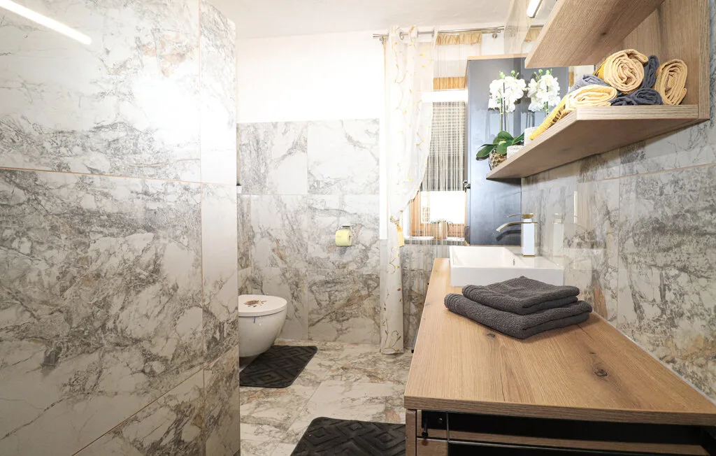 Un baño con un tocador, toallas dobladas y paredes con vetas de mármol.