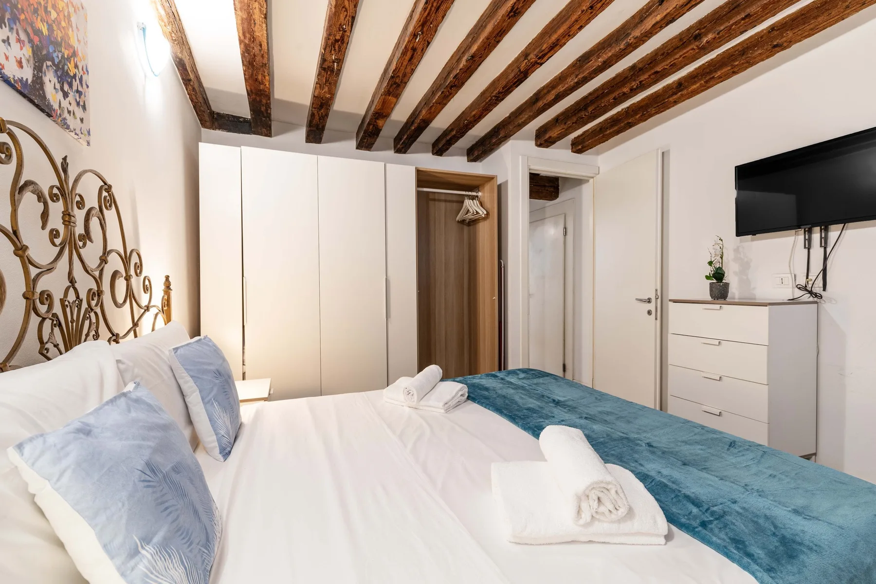 A bedroom with a white bed, blue bedspread, and wall-mounted television.
