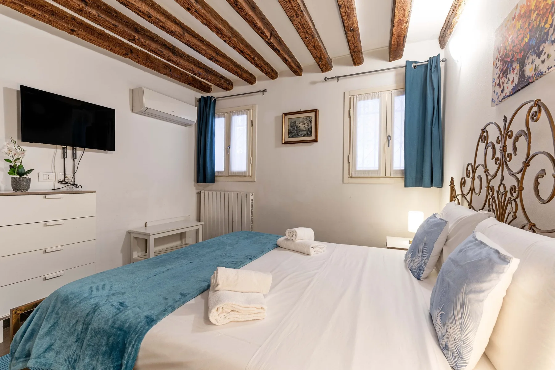 A bedroom with a bed, blue bedding, and exposed wooden ceiling beams.