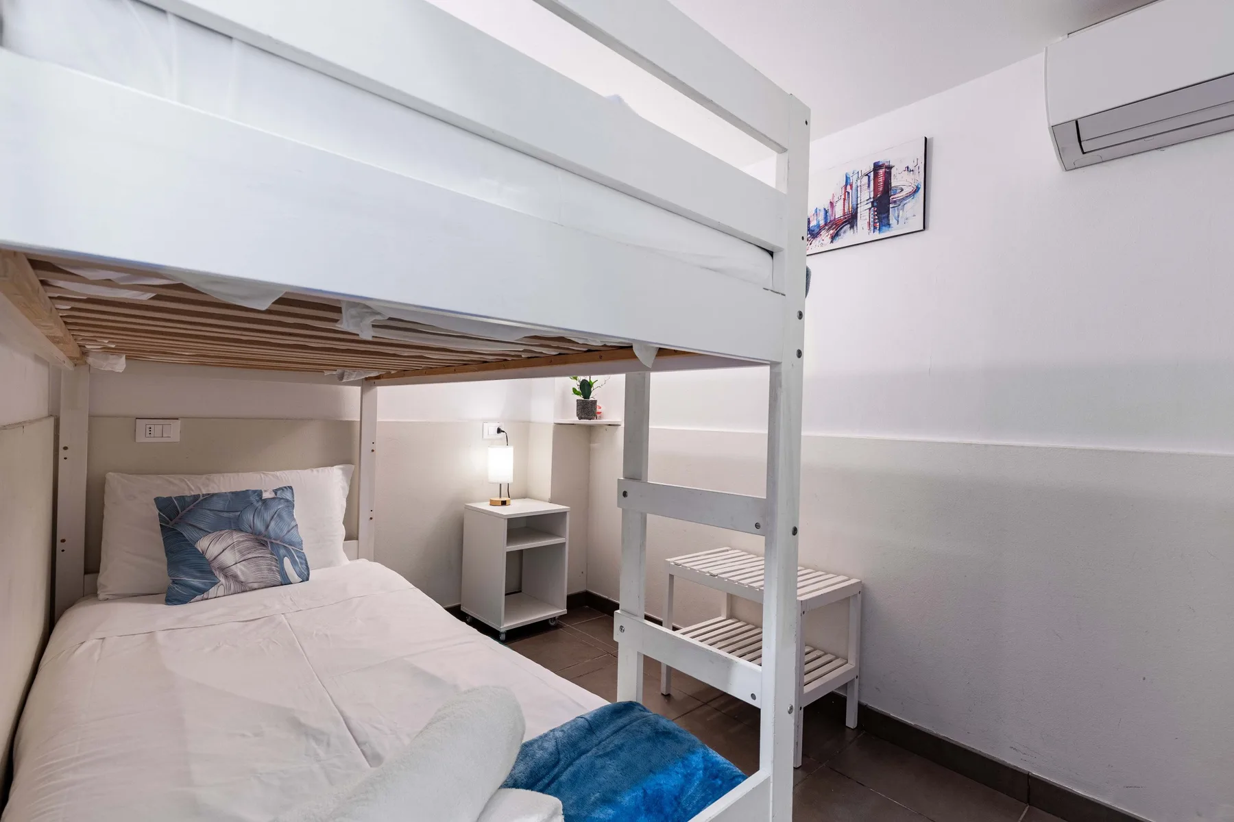 A bedroom with a raised bunk bed above a lower bed and a bedside table.