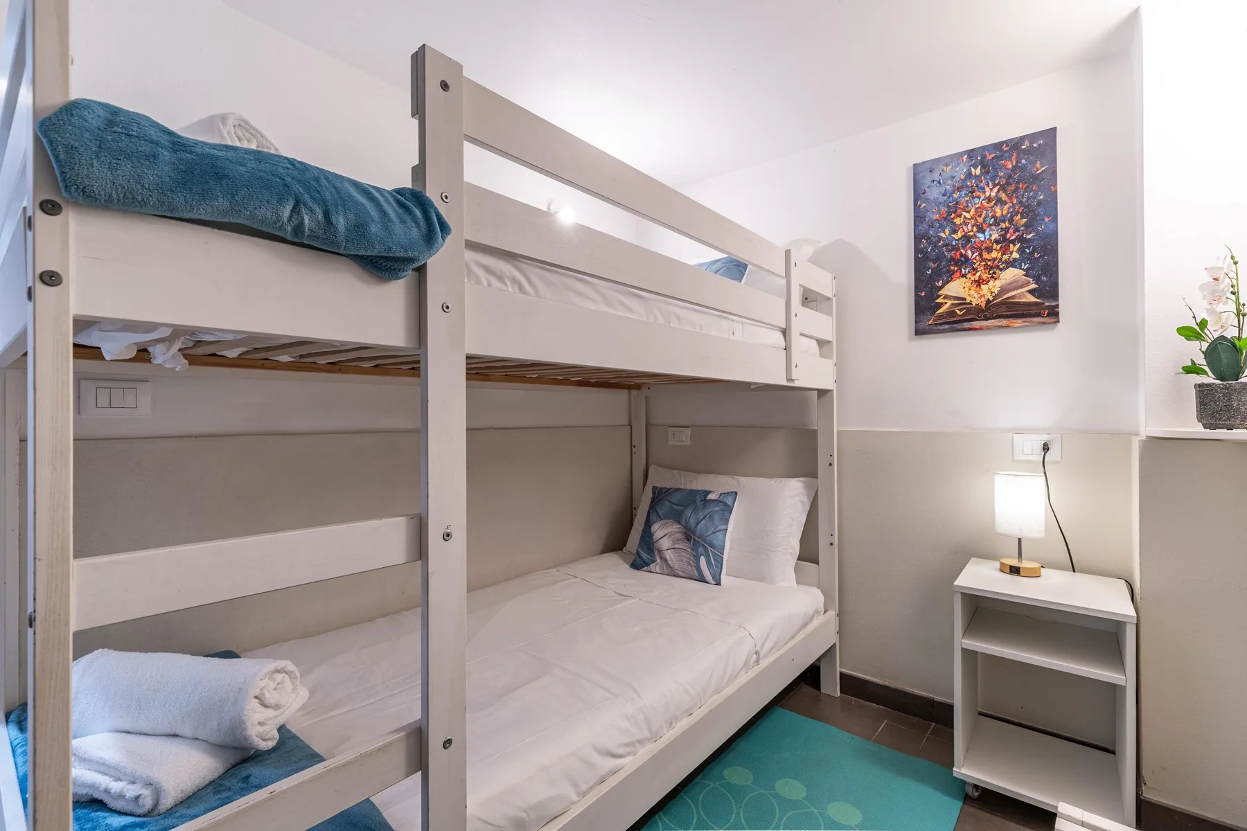 A bedroom with a bunk bed, bedside table, and colorful wall art.