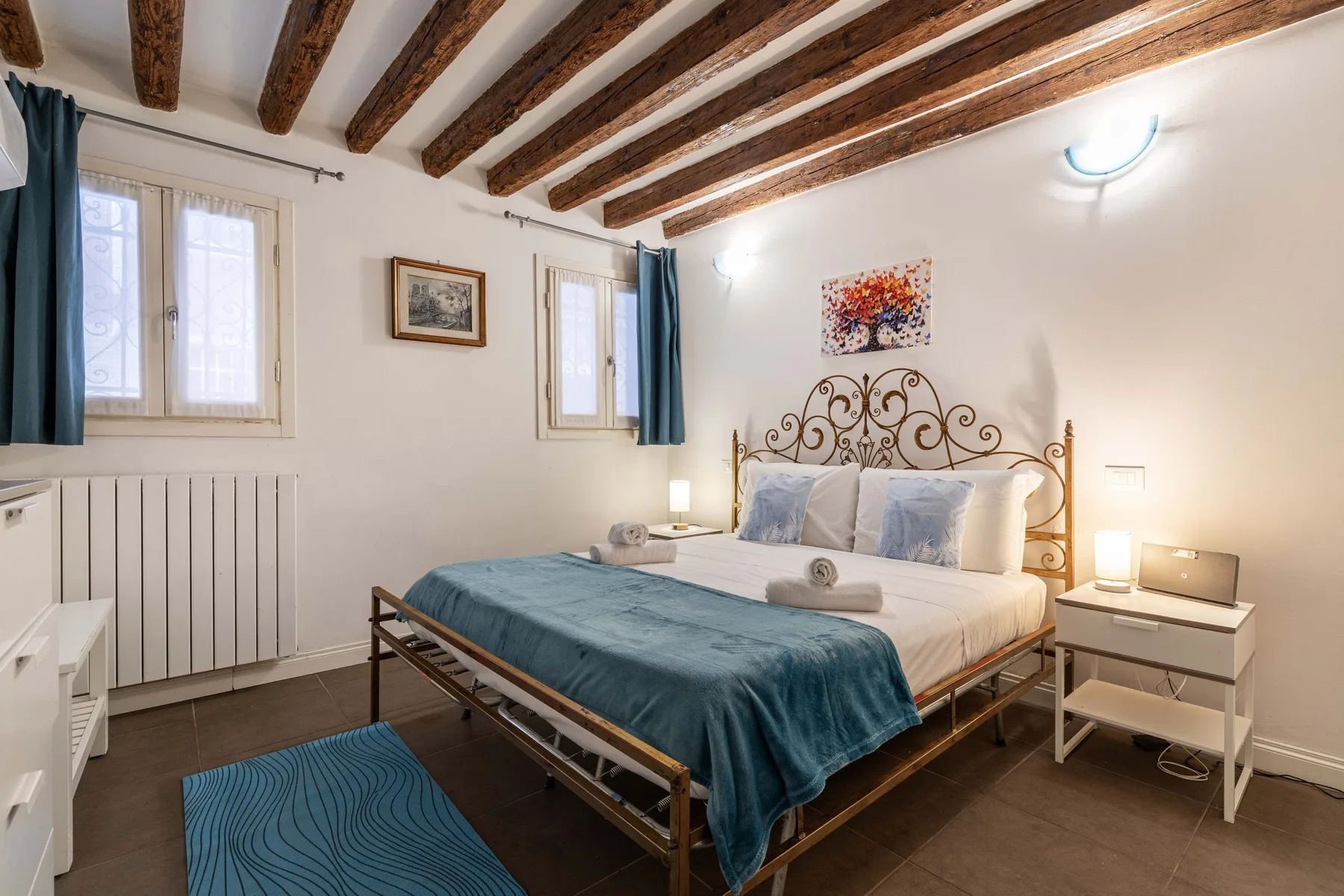 A bedroom with a metal bed, blue bedding, and exposed wooden ceiling beams.