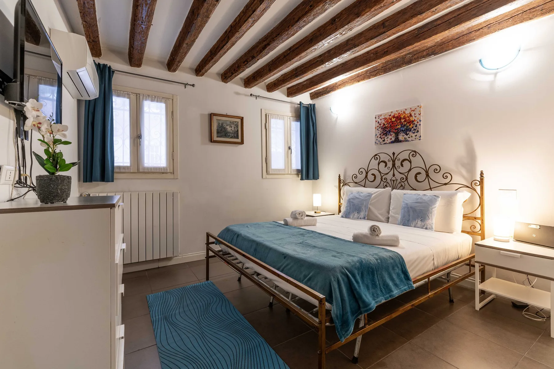 A bedroom with a metal bed, blue bedding, and exposed wooden ceiling beams.