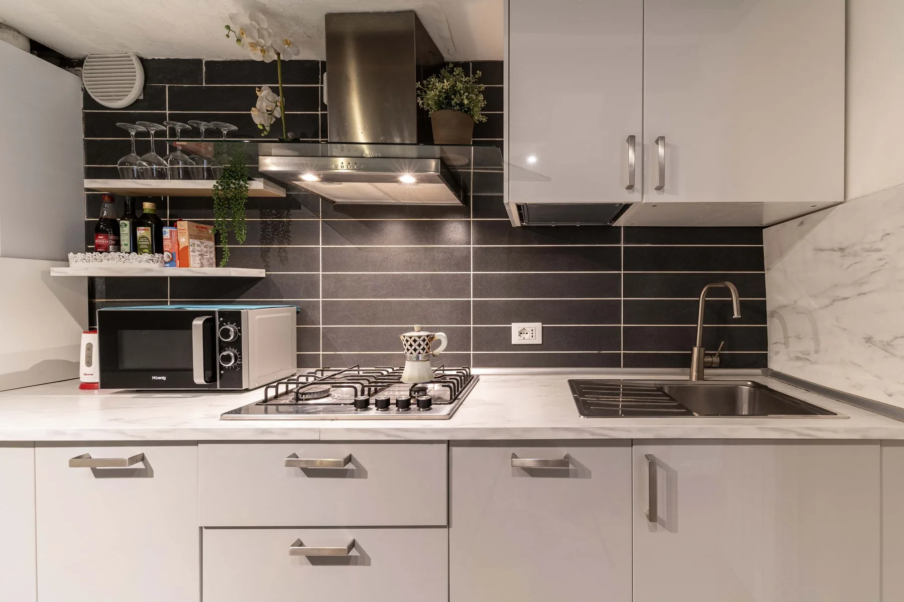A modern kitchen with white cabinets, a dark tiled backsplash, and a countertop.