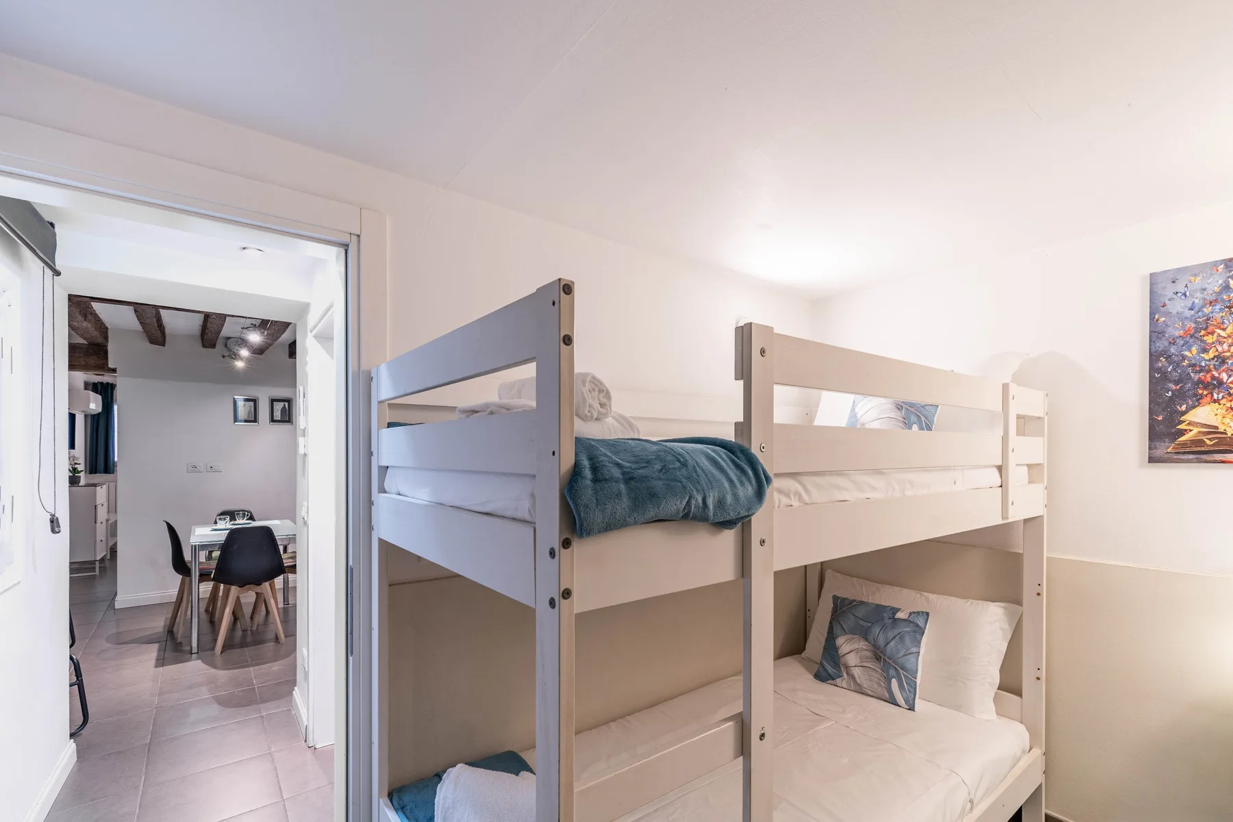 A bedroom with bunk beds and a small seating area visible through the doorway.