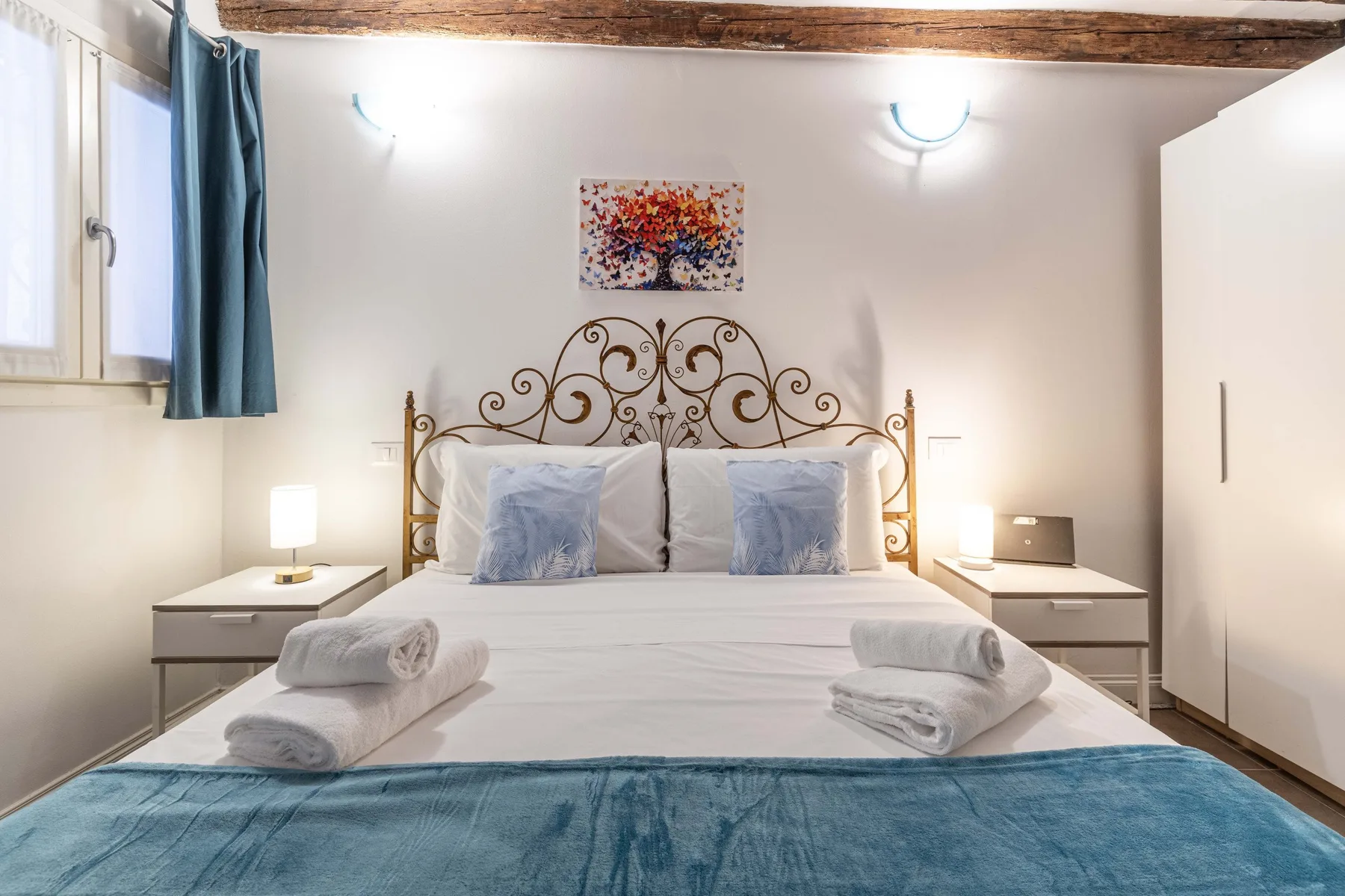 A bedroom with a double bed, decorative metal headboard, and blue curtains.