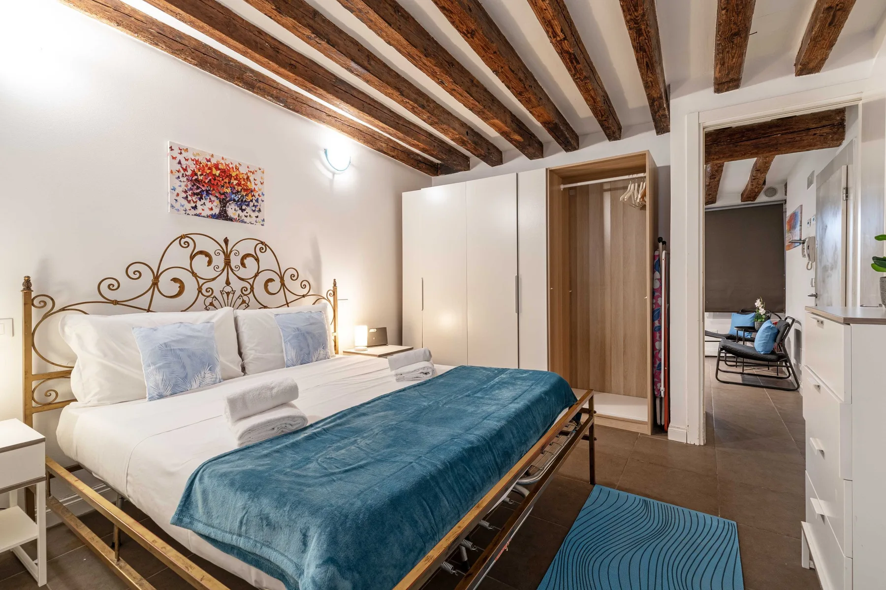 A bedroom with a bed, wardrobe, and exposed wooden ceiling beams.