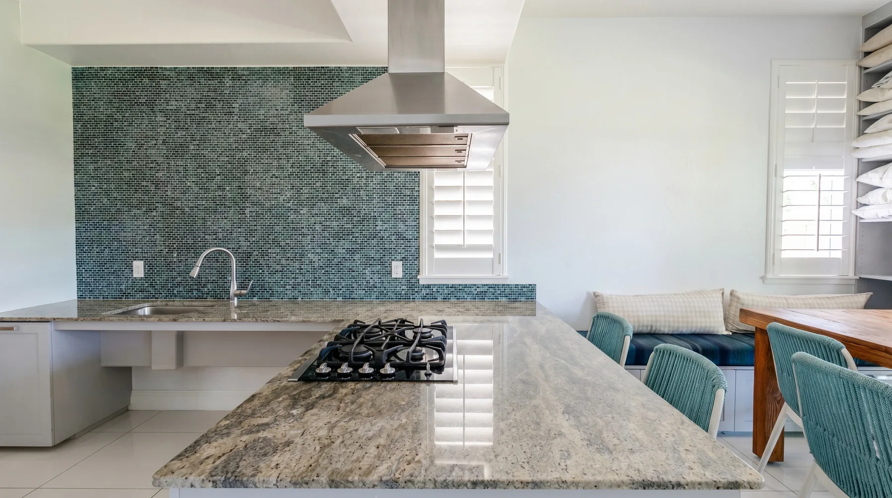A bright kitchen with a large island, cooktop, and green tiled backsplash.