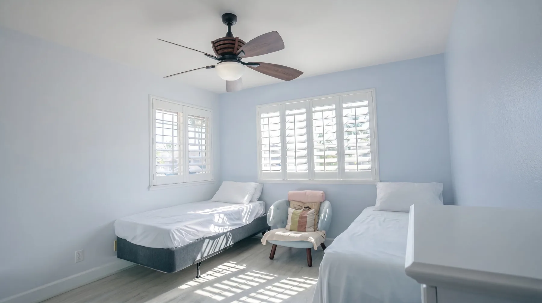 Un dormitorio luminoso con camas junto a ventanas con contraventanas.