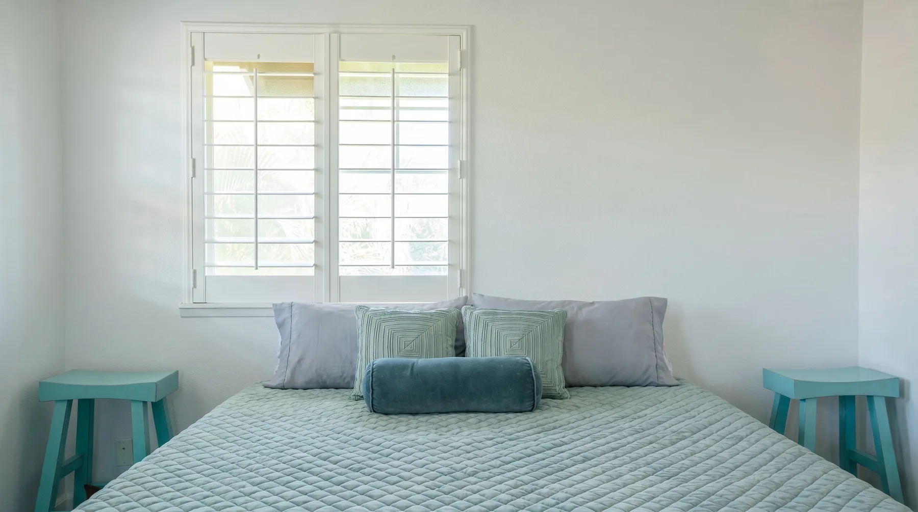 Un dormitorio con una cama acolchada bajo una ventana luminosa.