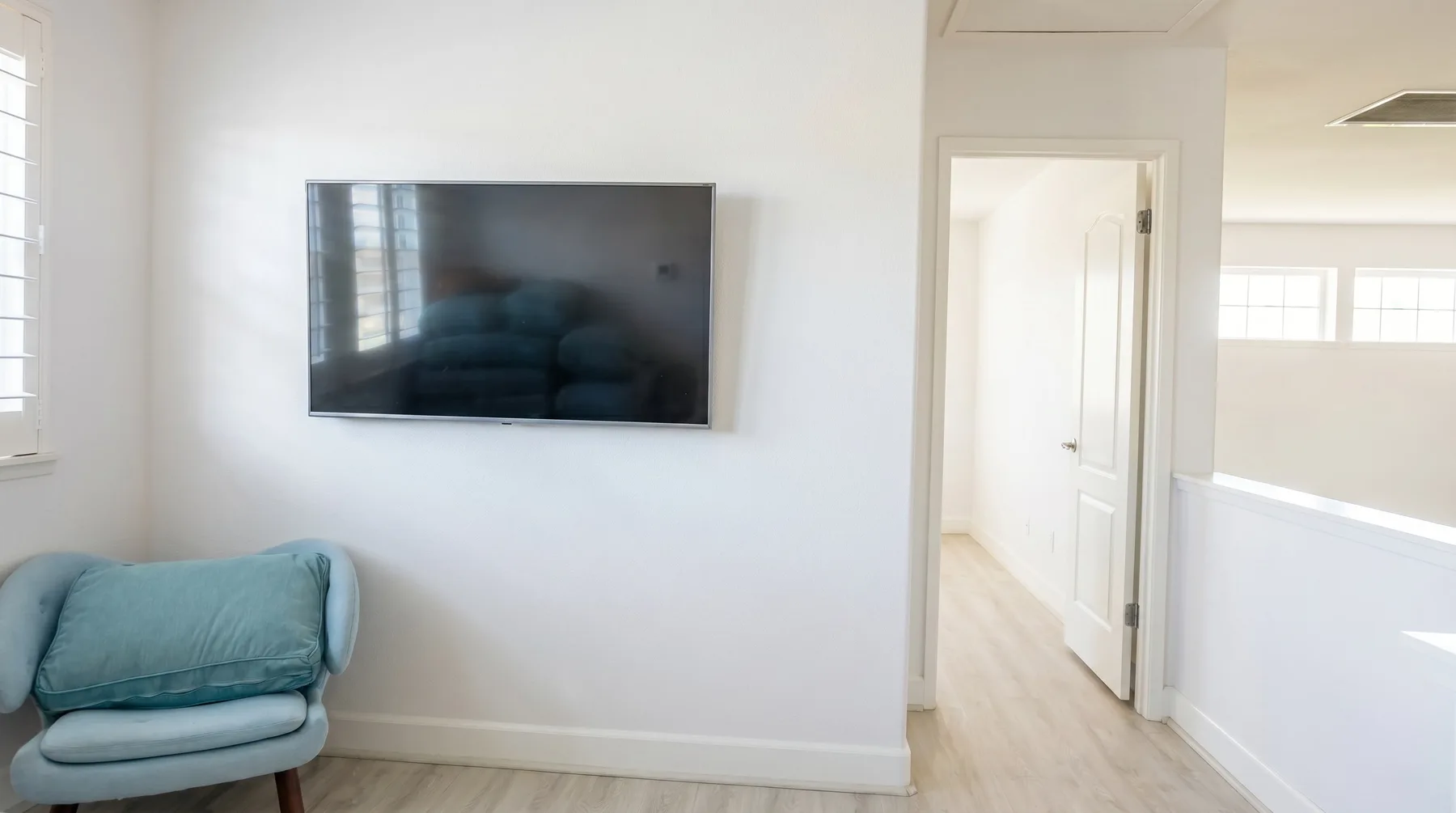 Un pasillo interior luminoso con un televisor en la pared y una puerta abierta.