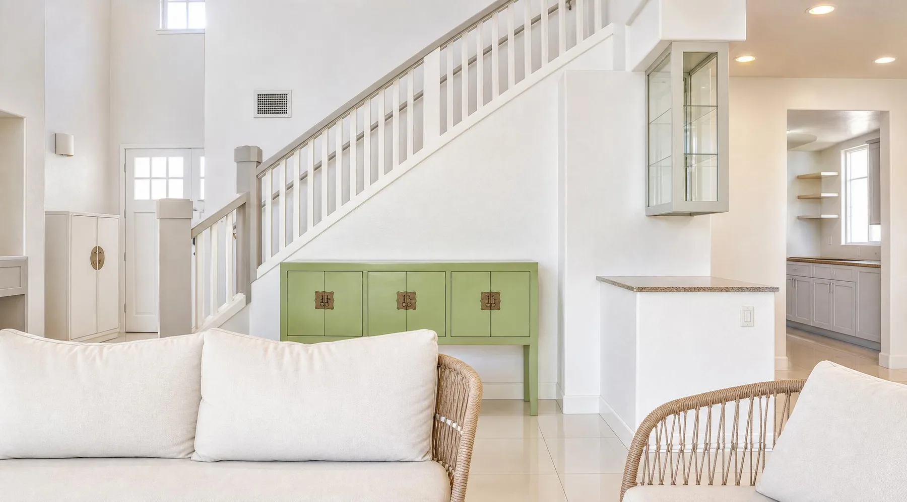 Una luminosa sala de estar con asientos blancos bajo una escalera y una consola verde.