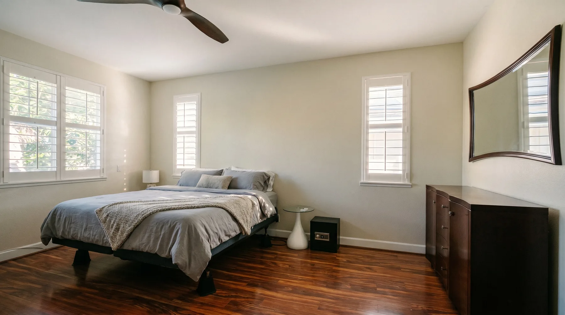Un dormitorio con una cama, varias ventanas y suelo de madera oscura.