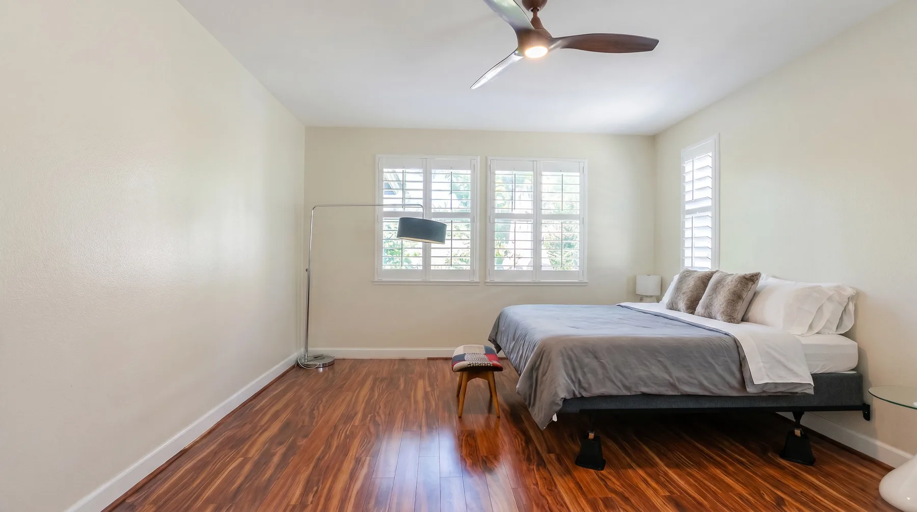 Un dormitorio luminoso con una cama, ventanas grandes y suelo de madera pulido.