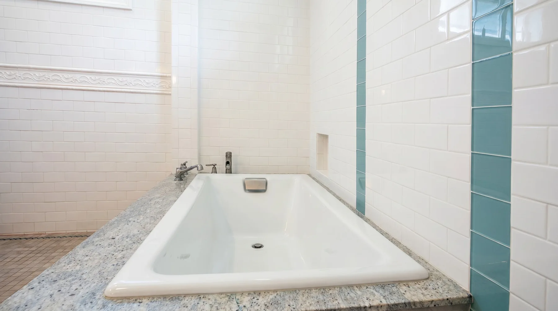 Una bañera en un baño con azulejos y una estrecha franja azul.