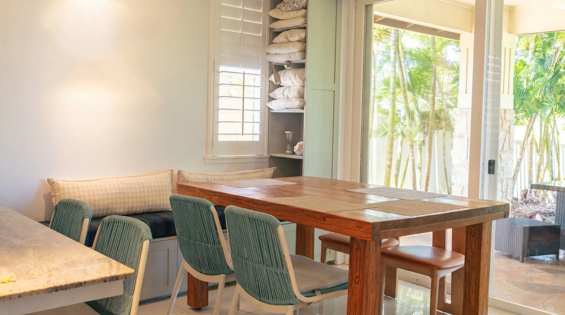 A bright dining area with a wooden table and green seating beside large windows.