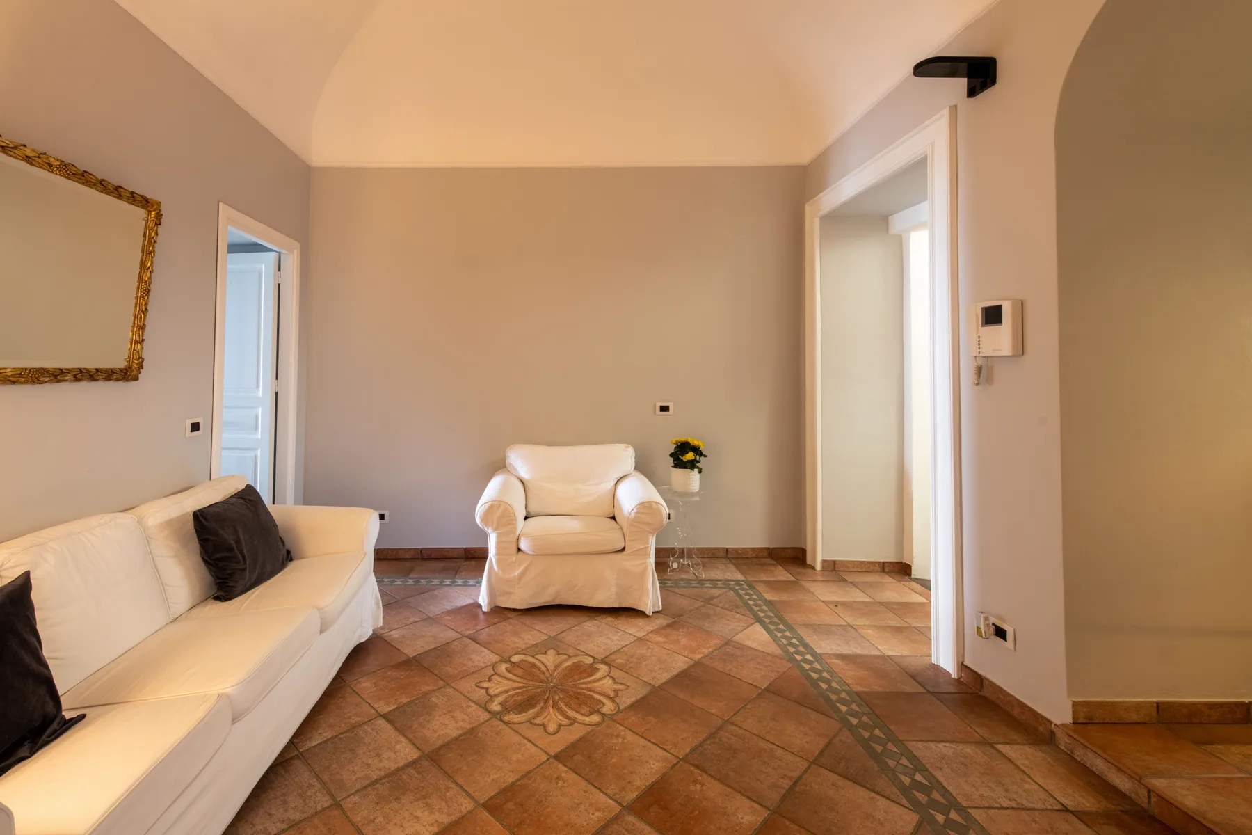 A living room with a white sofa and armchair on a patterned tile floor.