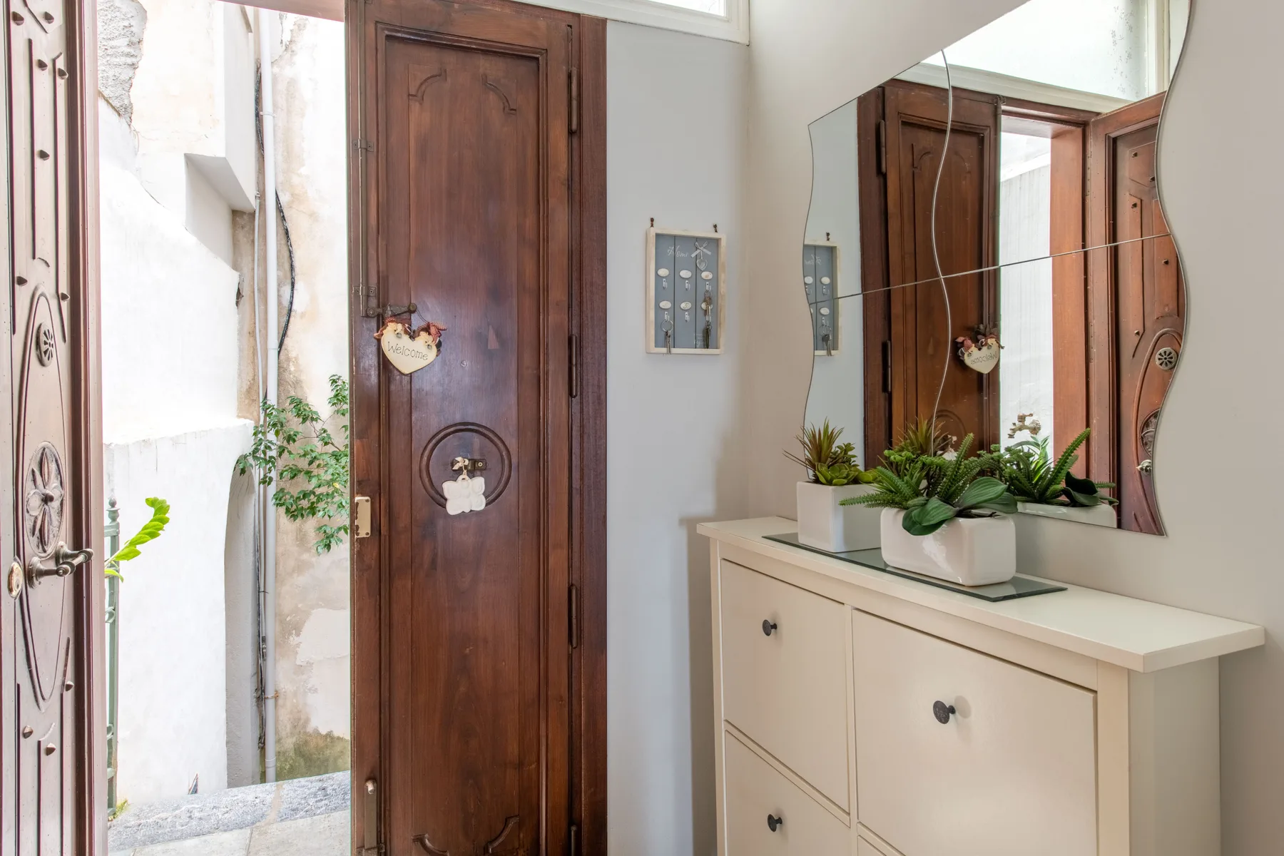 Un recibidor con una puerta de madera, una pared con espejo y un mueble blanco.