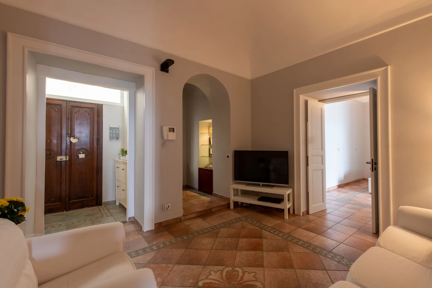 Una sala de estar con suelo de baldosas, asientos claros y un televisor.