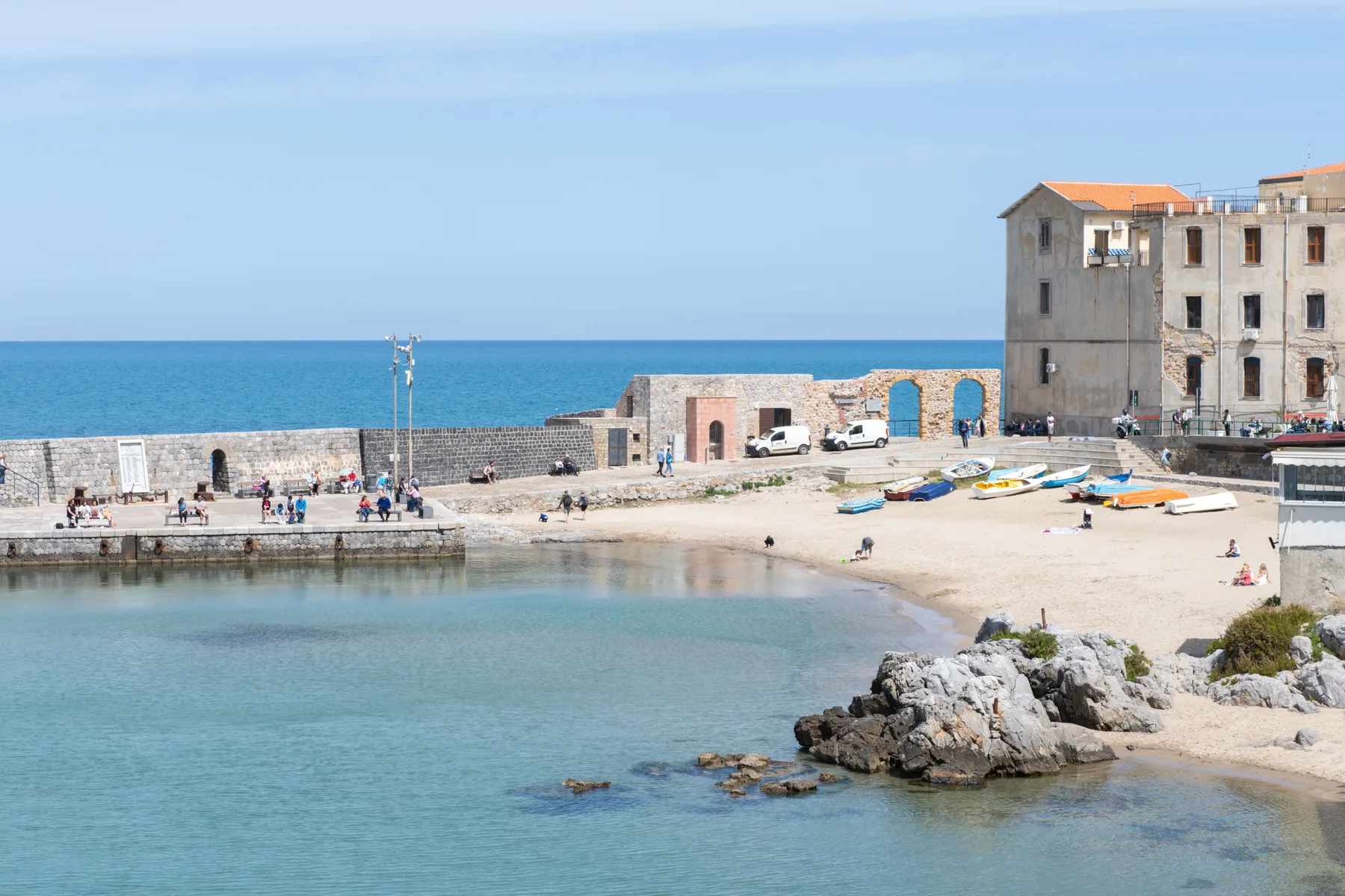 Un puerto junto al mar con aguas tranquilas, una orilla rocosa y edificios frente al agua.