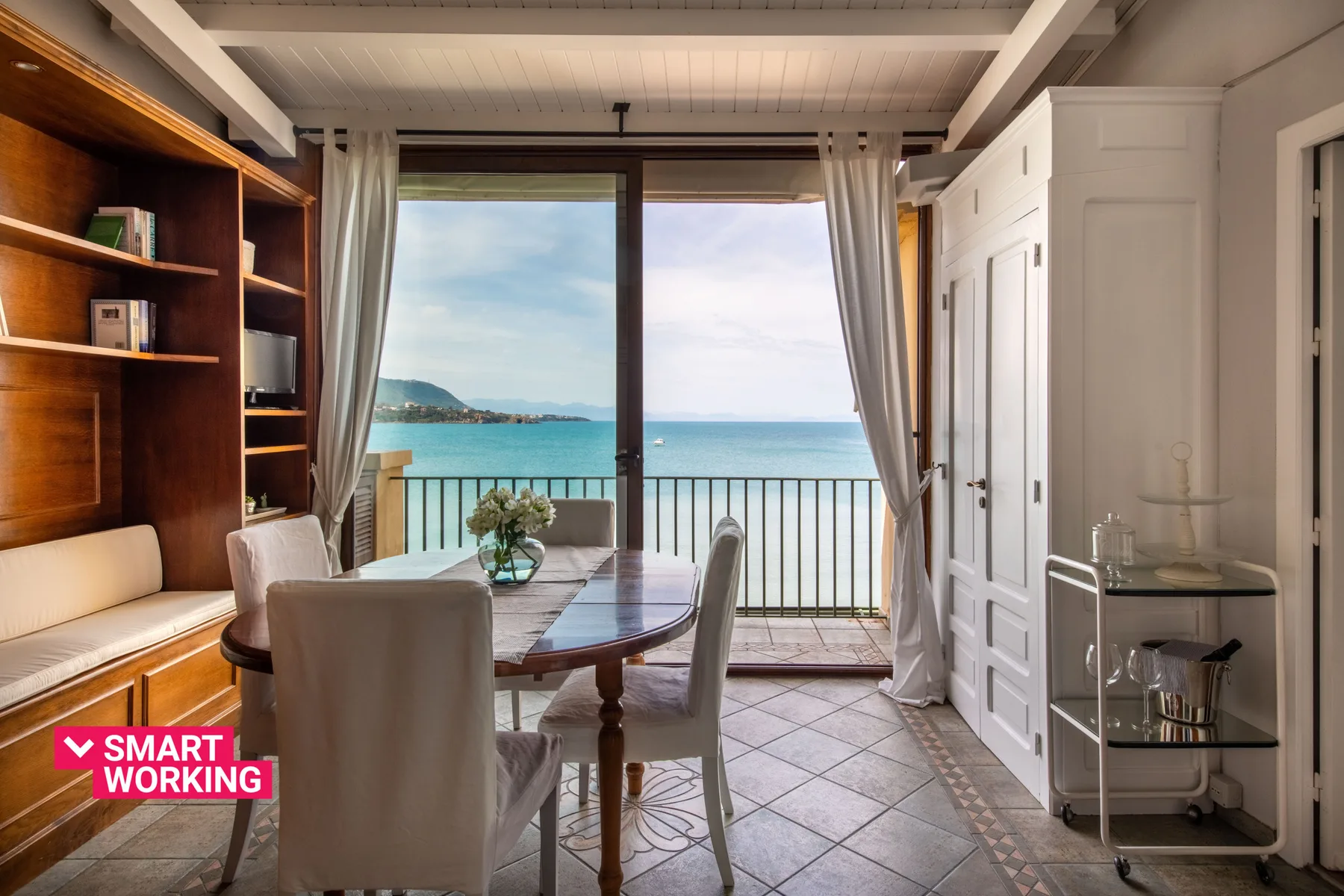 A dining area with a table and seating faces a large window overlooking the sea.