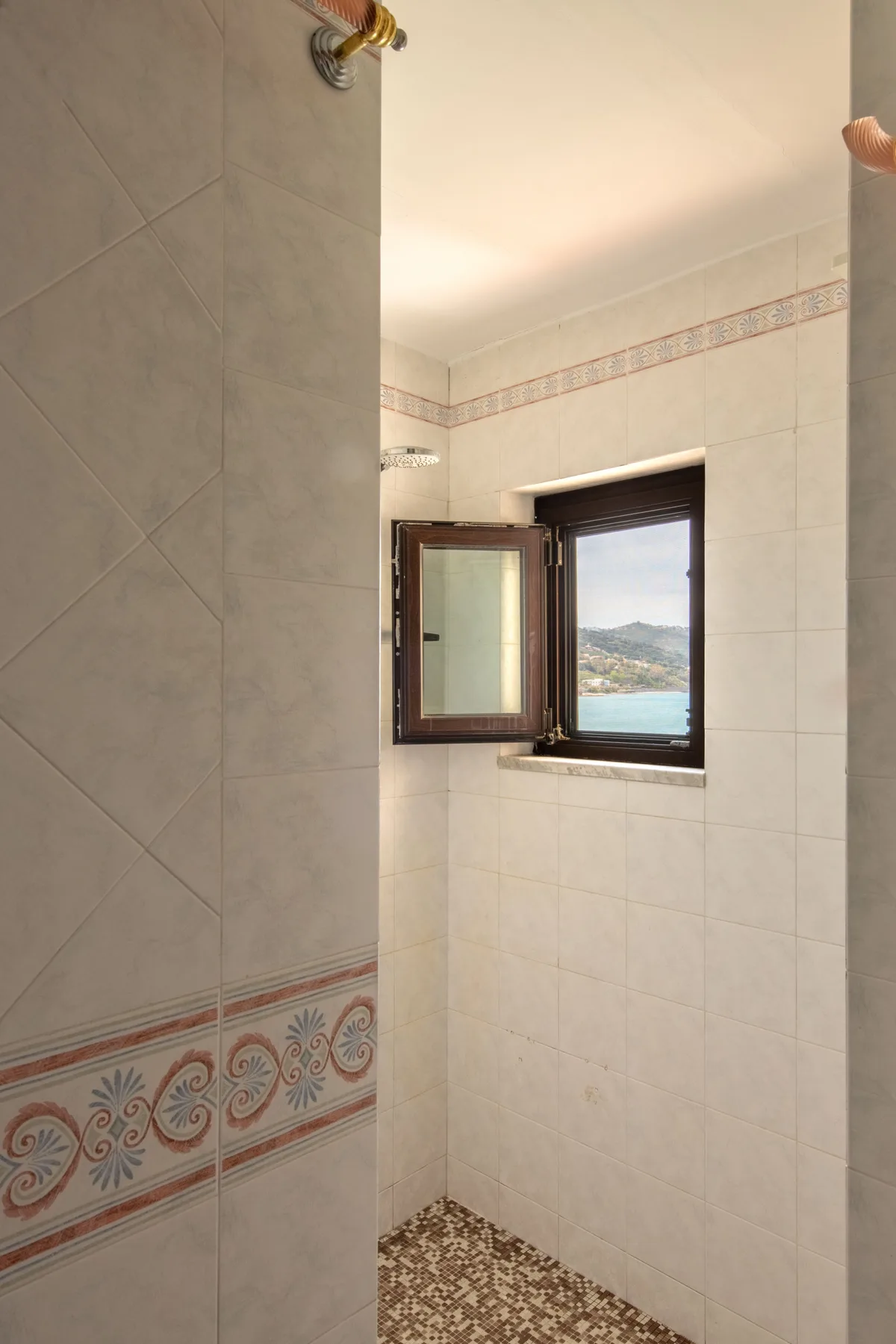 Un baño alicatado con una ventana abierta que da a un paisaje costero.