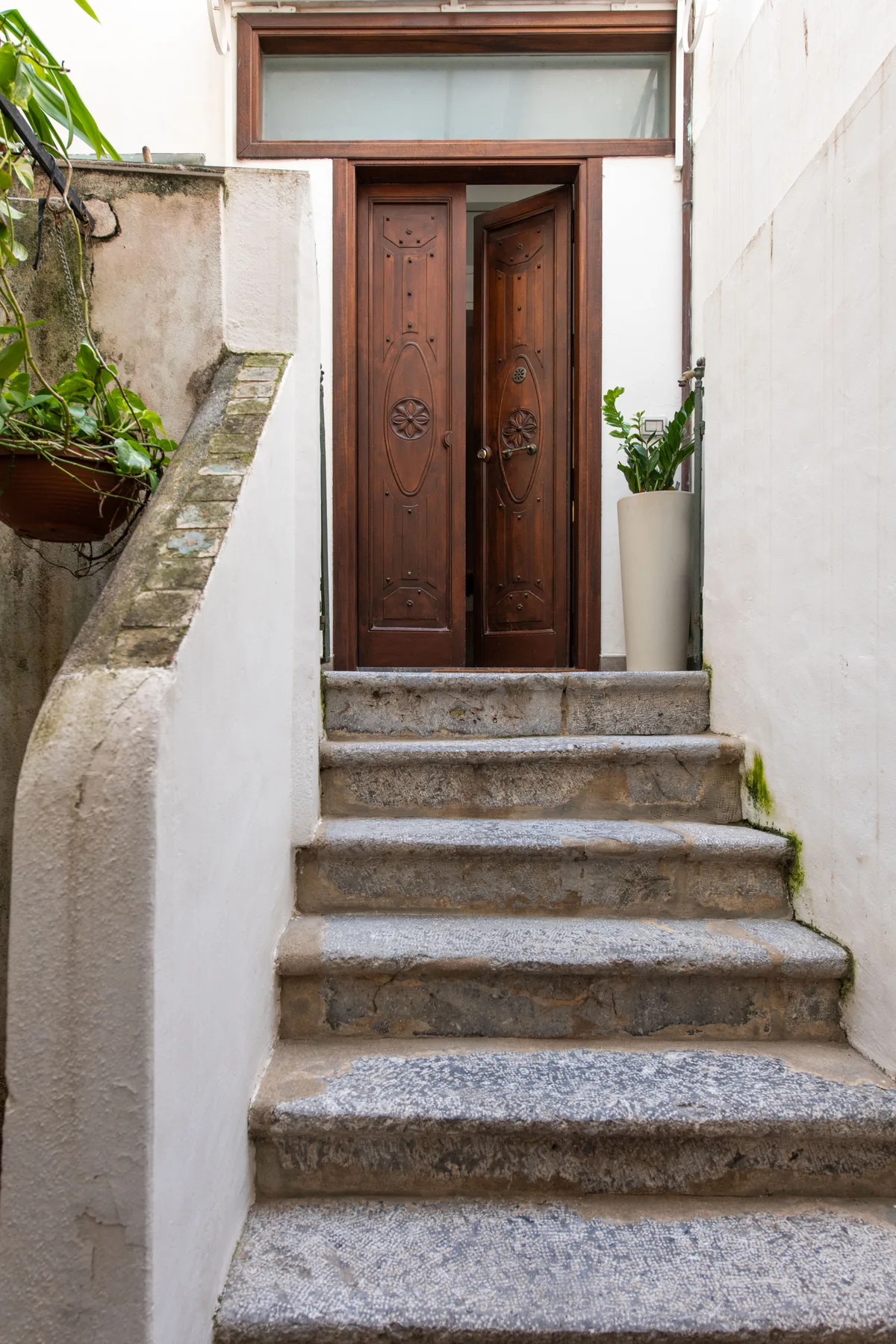 Escalones de piedra conducen a una puerta de madera ornamentada entre paredes blancas.
