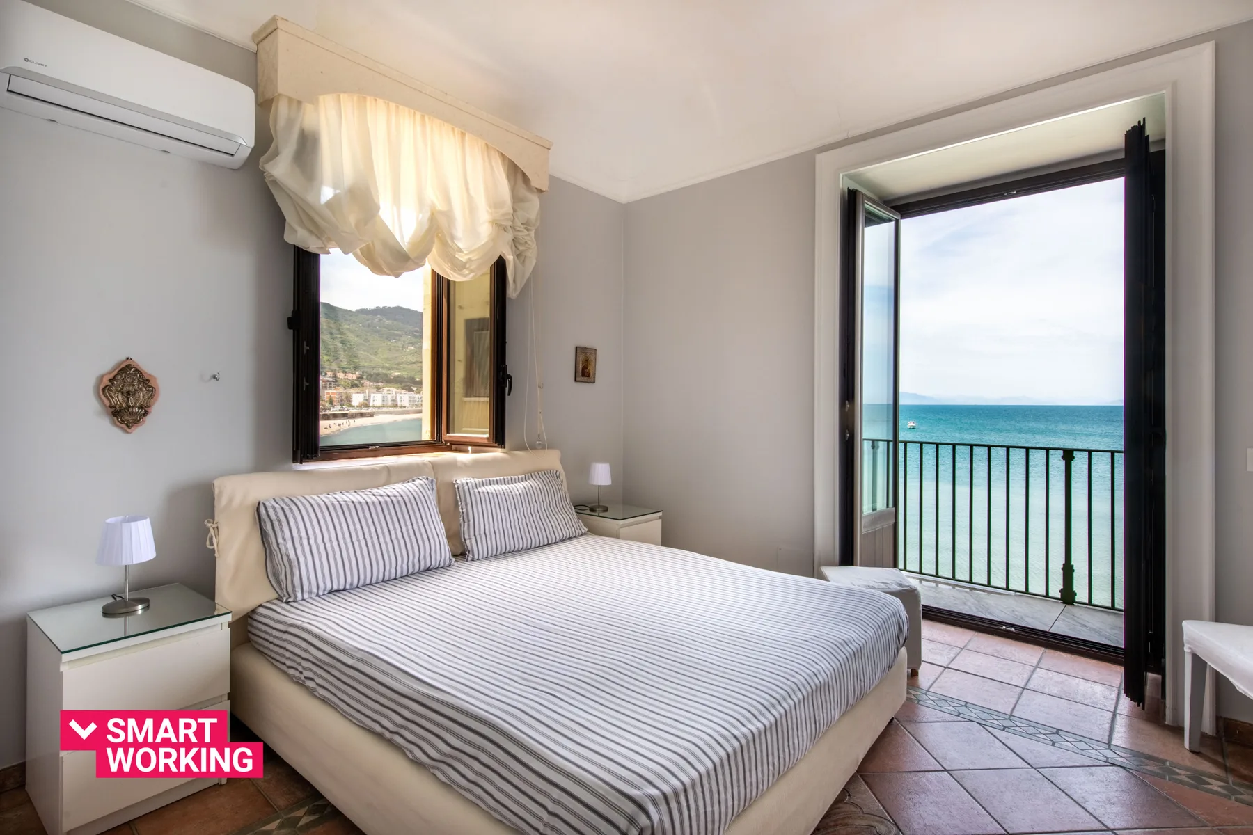 A bedroom with a striped bed beside open doors overlooking the sea.