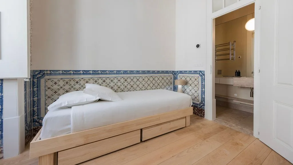 Un dormitorio con una cama baja junto a una pared de azulejos y una puerta abierta.