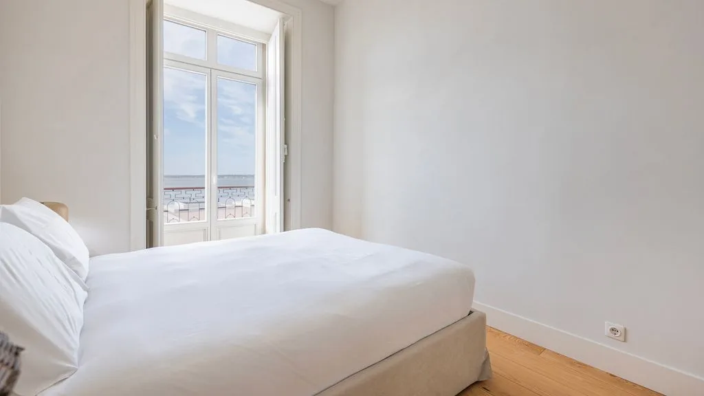 Un dormitorio luminoso con una cama junto a una ventana alta.
