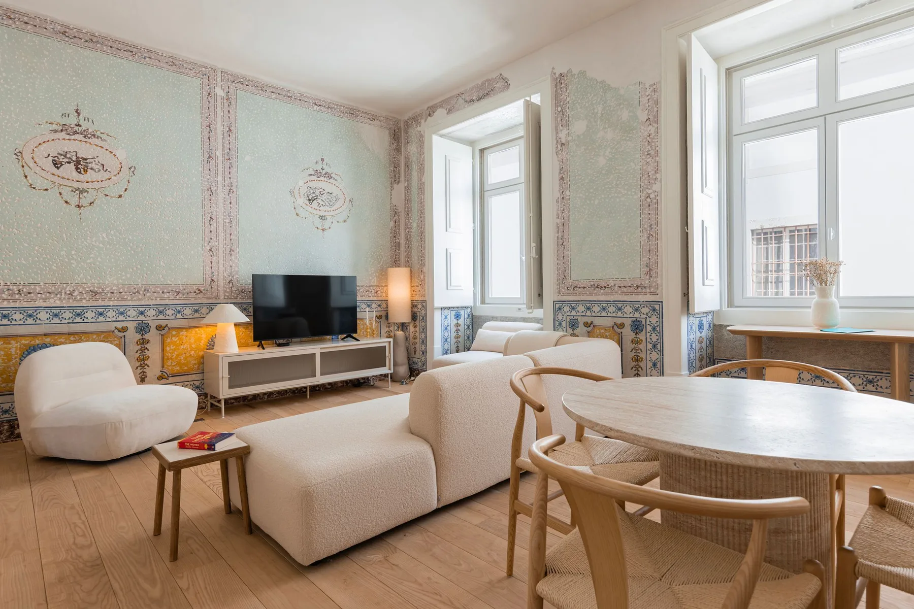 Una sala luminosa con asientos, un televisor y una mesa de comedor junto a las ventanas.