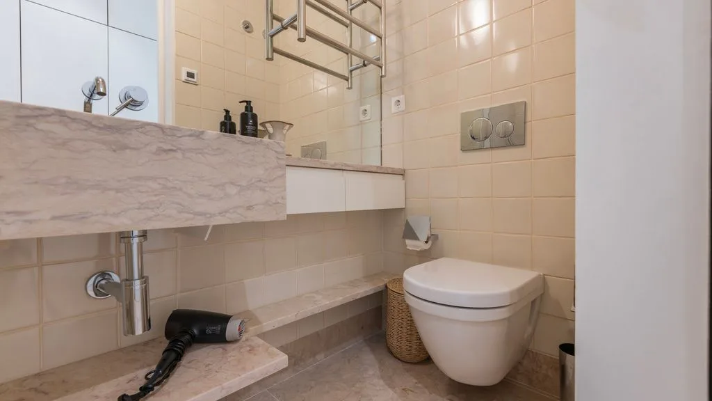 Un baño con azulejos, lavabo suspendido, inodoro y secador de pelo.
