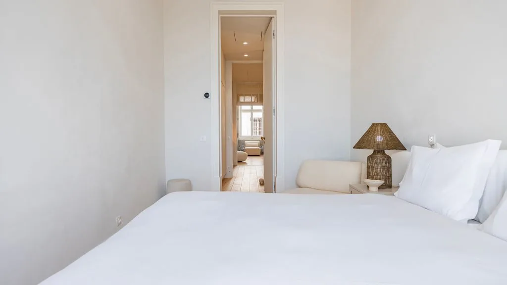 Un dormitorio luminoso con una cama bien tendida y una lámpara al lado.