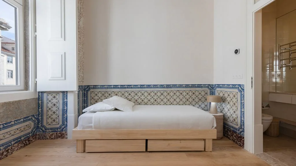Un dormitorio con una cama baja junto a una pared con azulejos estampados.