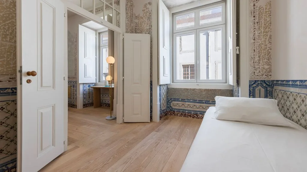 Un dormitorio luminoso con una cama junto a una ventana grande y una puerta abierta.