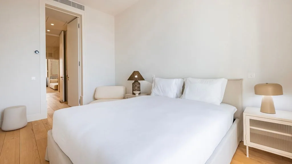 Un dormitorio luminoso con una cama grande y una puerta que da a un pasillo.