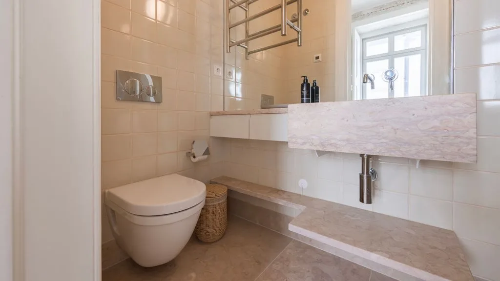 Un baño revestido de azulejos con inodoro, lavabo suspendido y ventana.