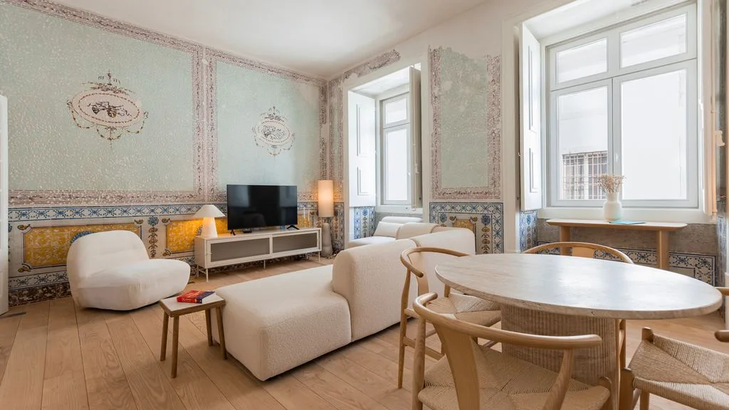 Una sala luminosa con asientos y una mesa de comedor redonda junto a grandes ventanas.