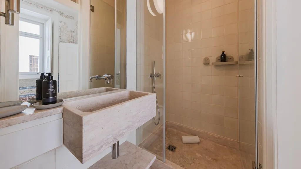 Un baño con azulejos, lavabo de piedra y ducha con mampara de vidrio.
