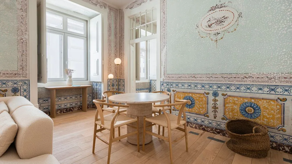 Un comedor con una mesa de madera y sillas junto a ventanas altas.