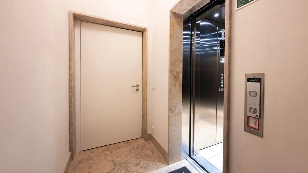 Un pasillo interior con una puerta cerrada junto a un ascensor abierto.