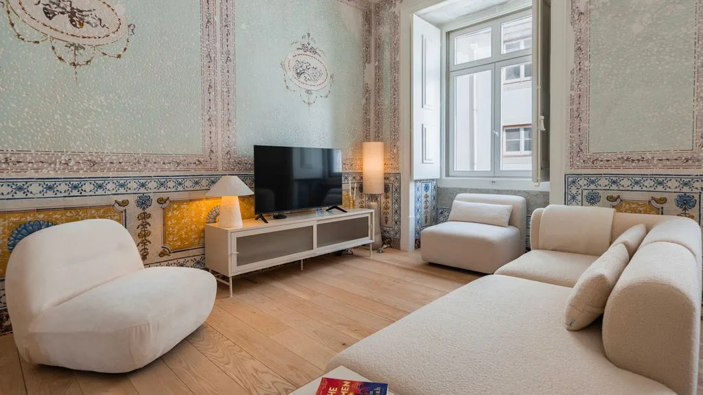 Una sala luminosa con asientos claros, un televisor y una ventana grande.