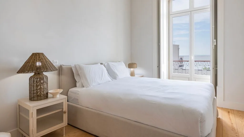 Un dormitorio luminoso con una cama bien tendida junto a una ventana alta.