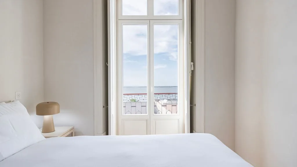 Un dormitorio con una cama tendida junto a ventanas altas con vistas al mar.
