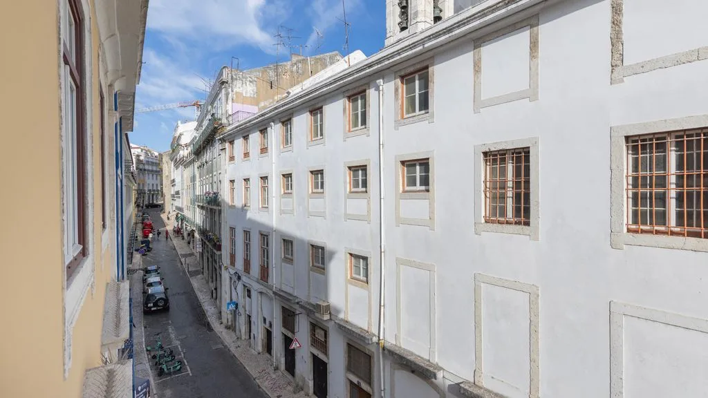 Una calle estrecha pasa entre edificios claros, con coches estacionados abajo.