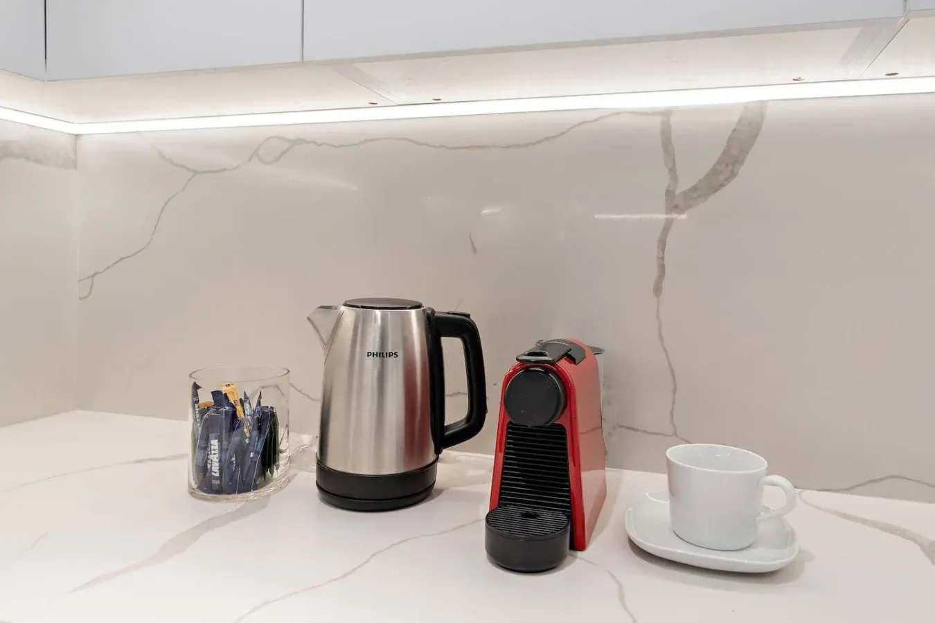 Una encimera de cocina con una tetera, una cafetera y una taza.